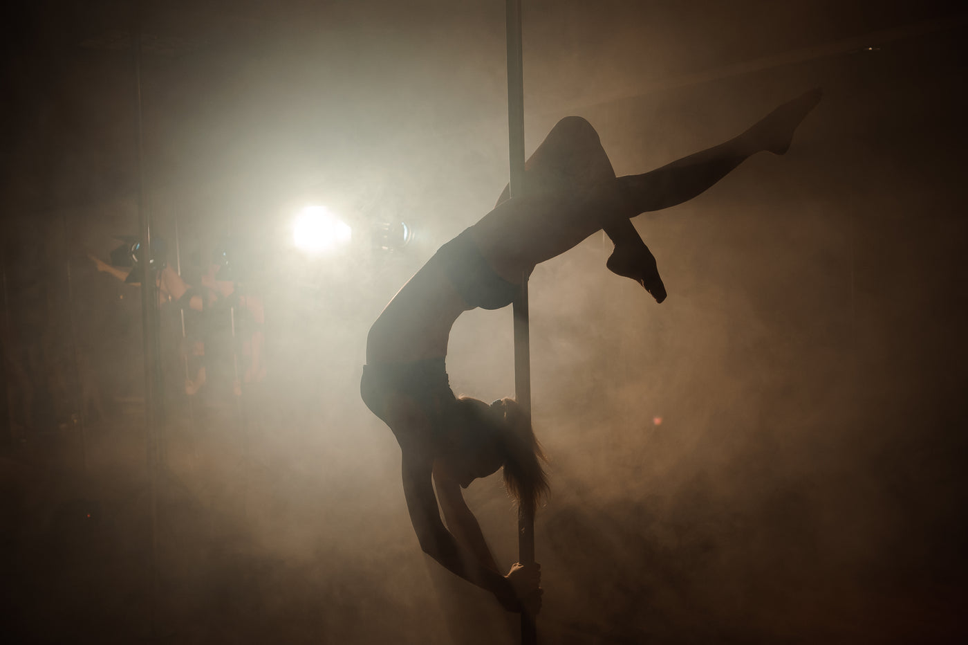 silhouette of artist doing an inverted back bend on a dance pole